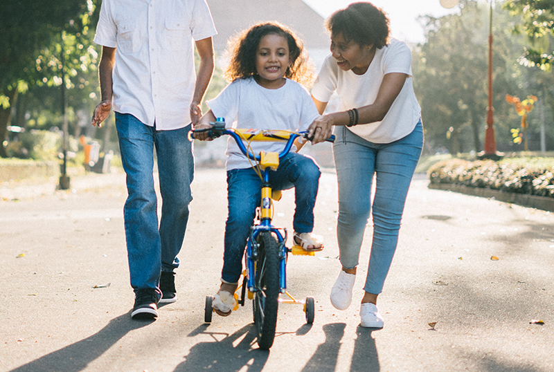 Girl on a bike with her mom helping her learn to ride