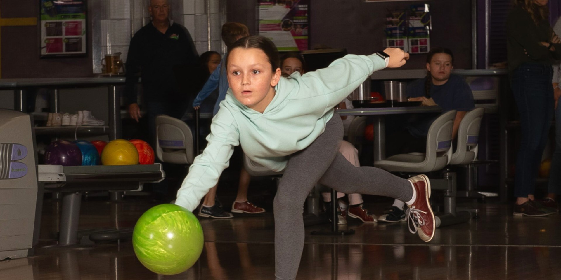 Young girl releasing a green bowling ball down the lane